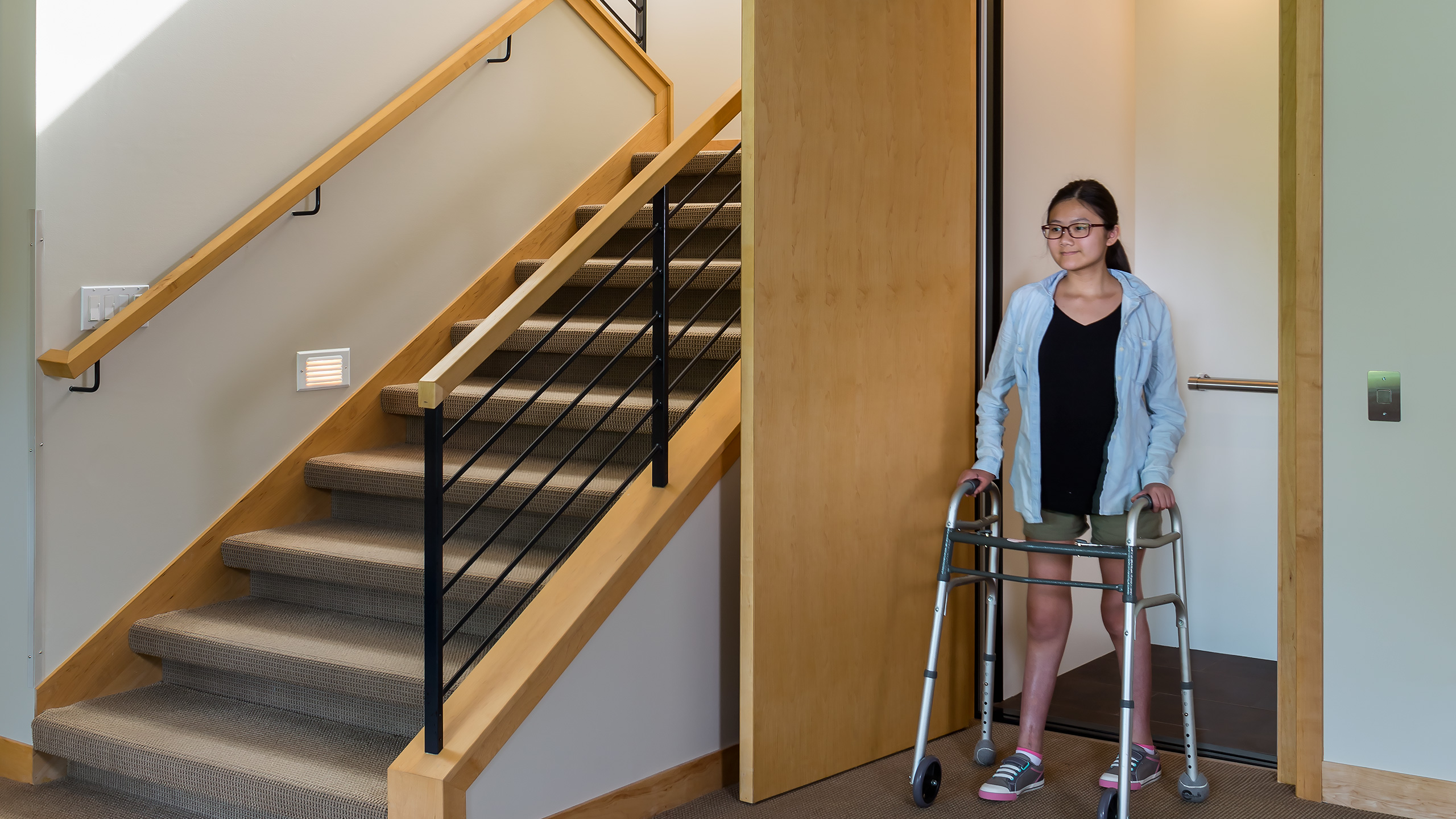 Girl with walker coming out of elevator door next to a set of stairs