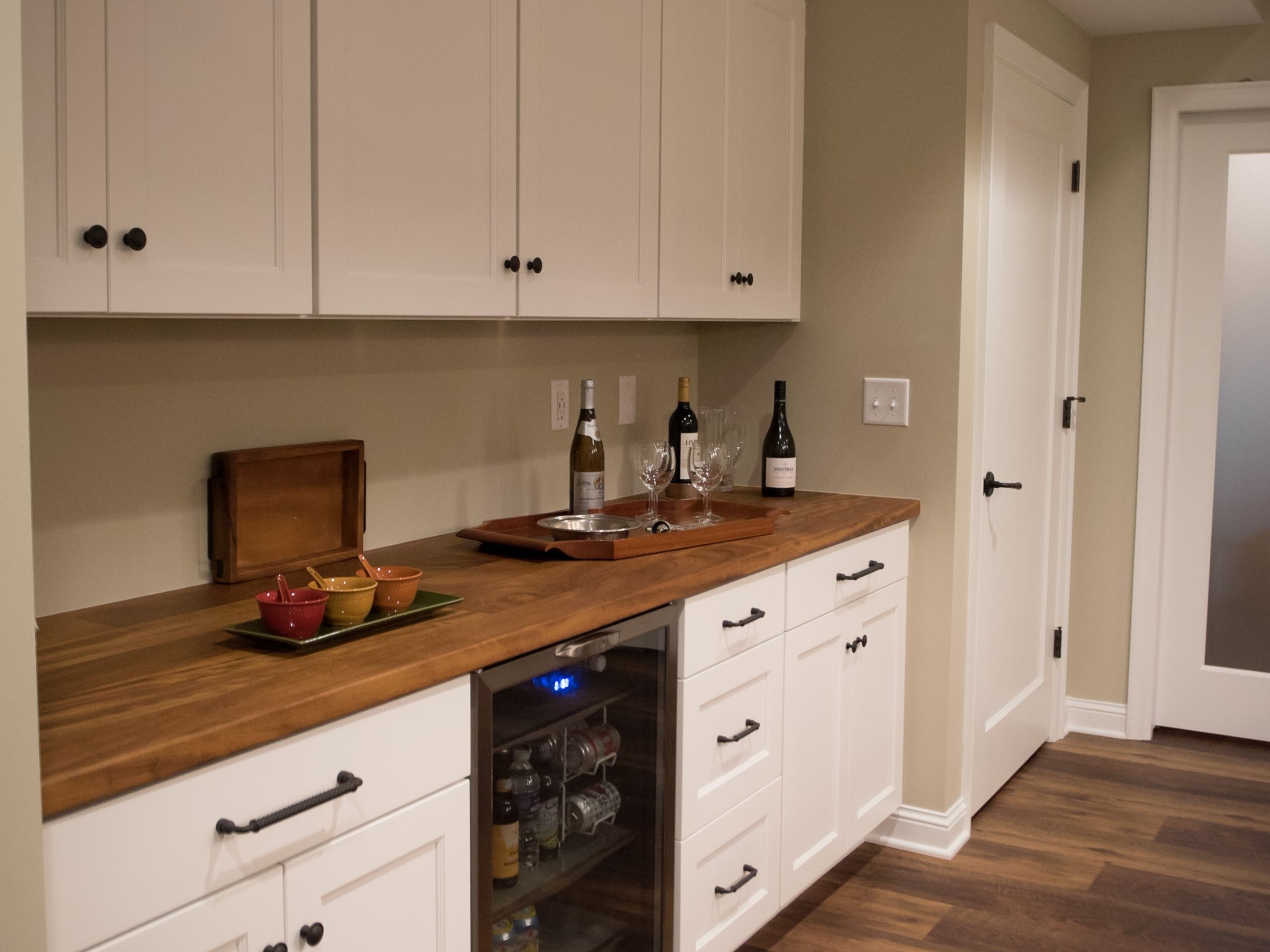 basement remodeling ideas: Basement bar area with wine fridge, white cabinets and wine and glasses on counter