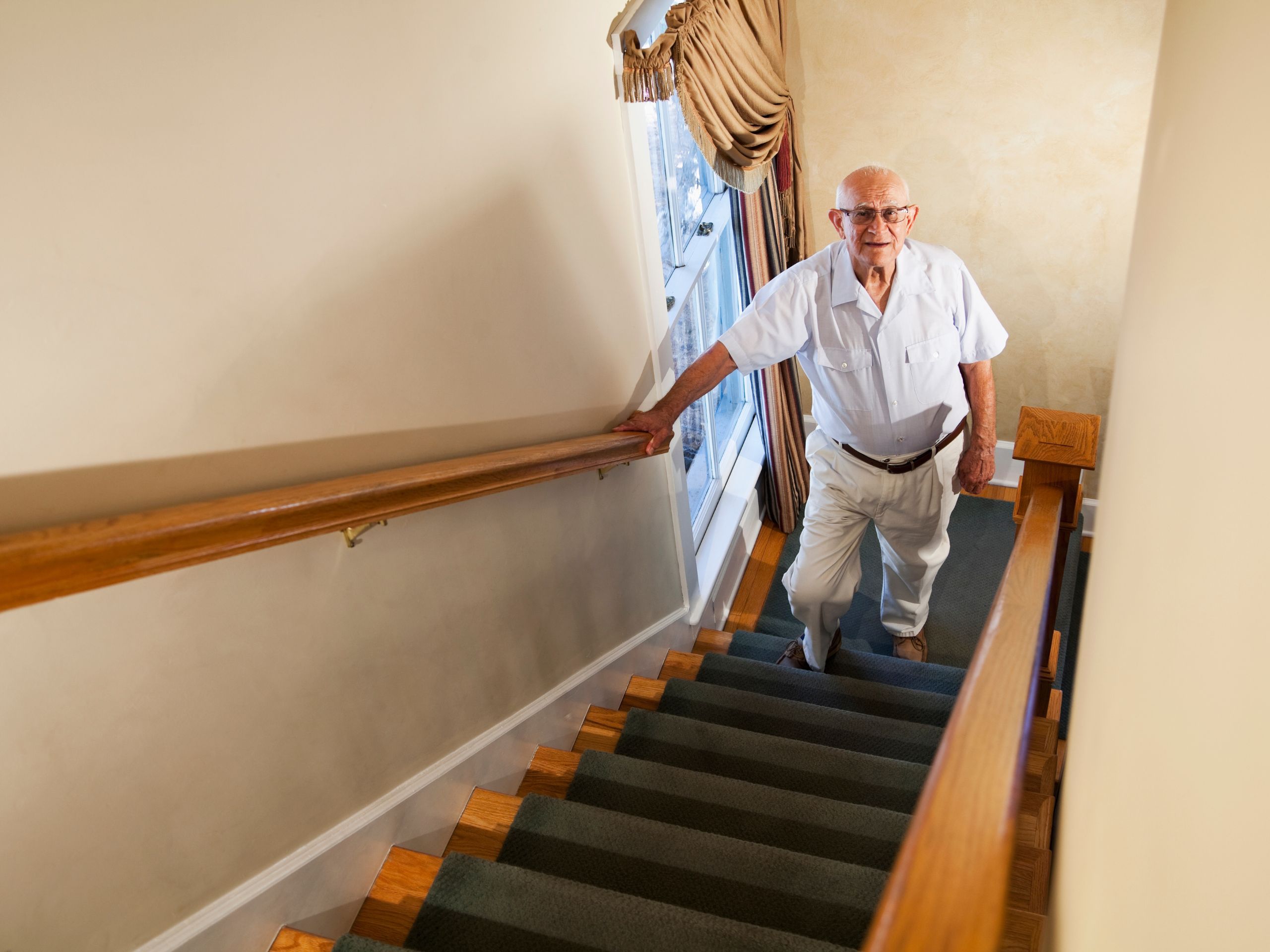 Elderly man at the bottom of a set of stairs looking to walk up holding onto handrail