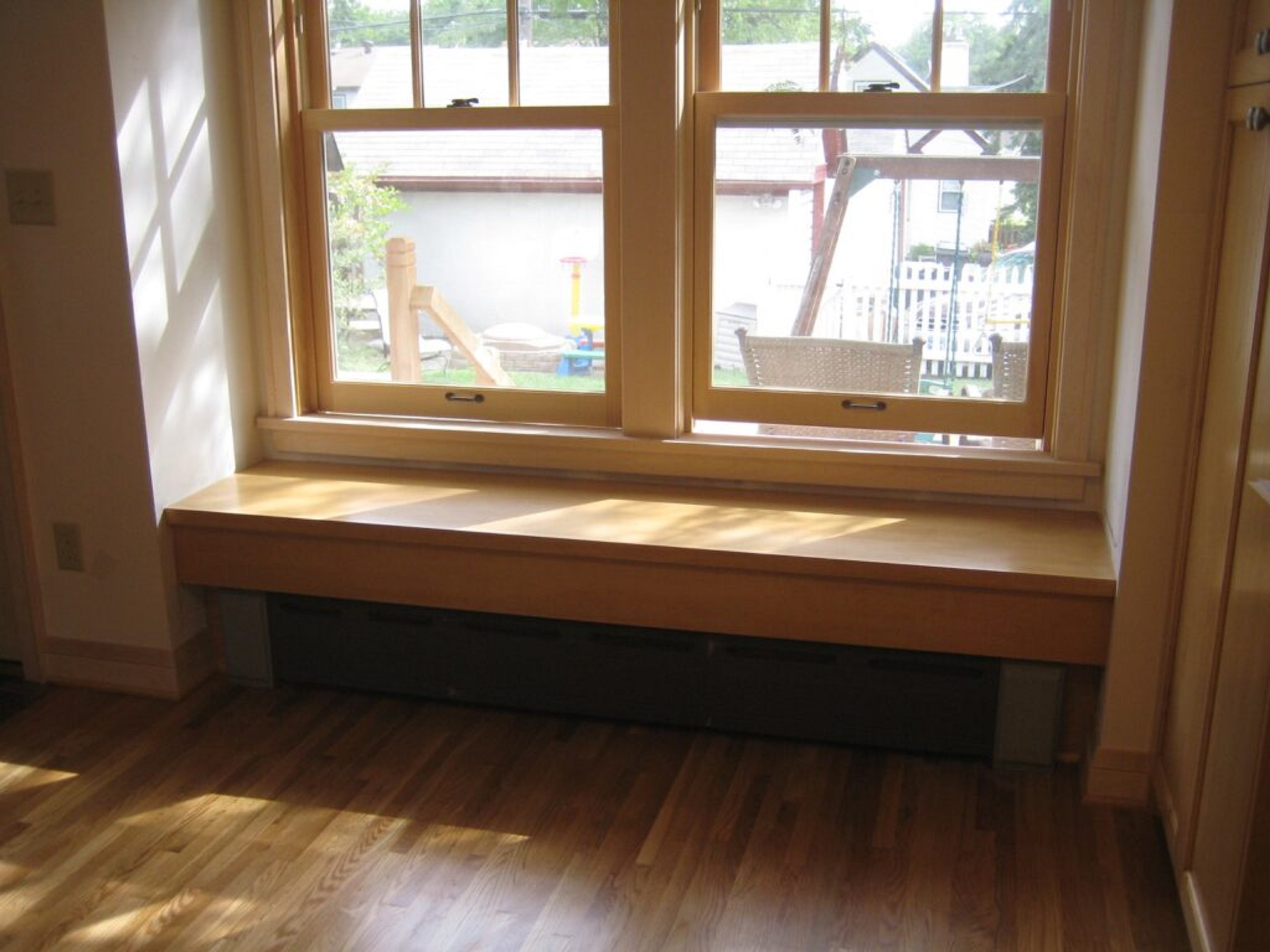 A wooden bench under a window with storage space underneath the bench. 