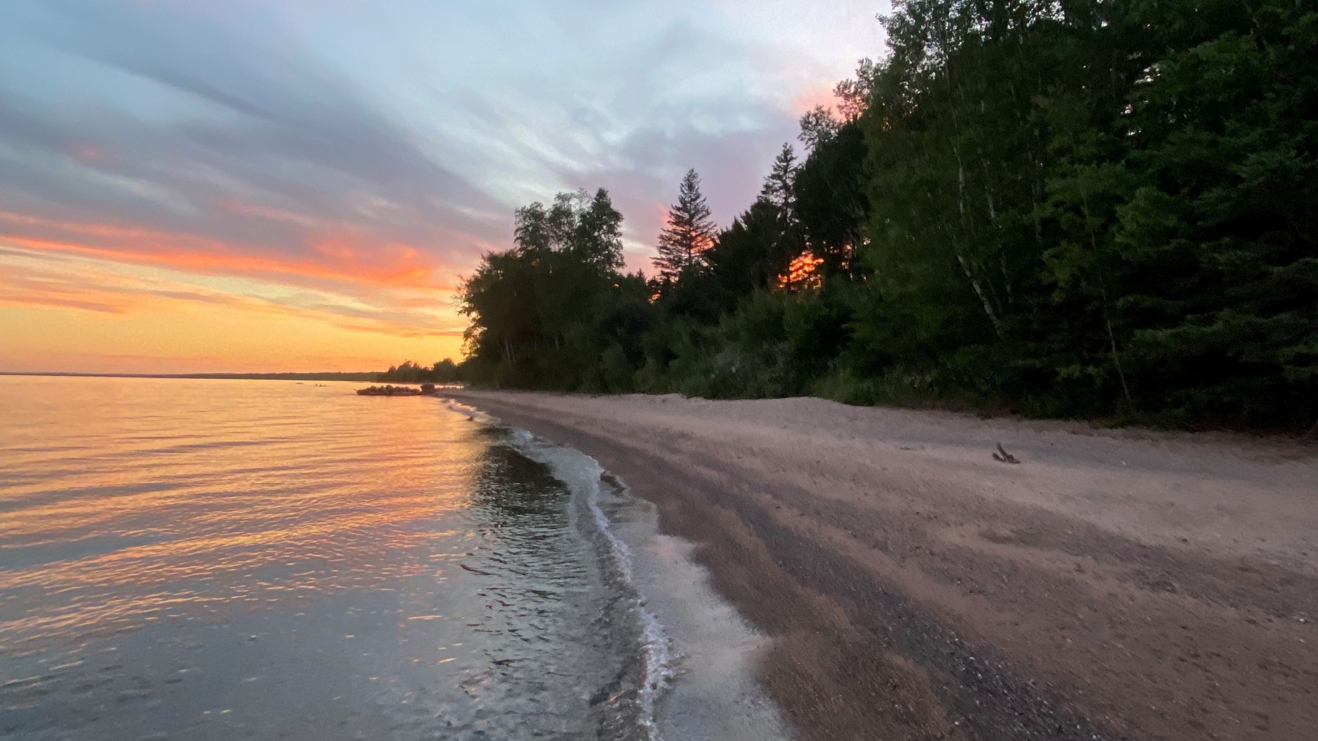 what's the story - red and yellow sunset over water on sandy lake beach, trees and blue clouds