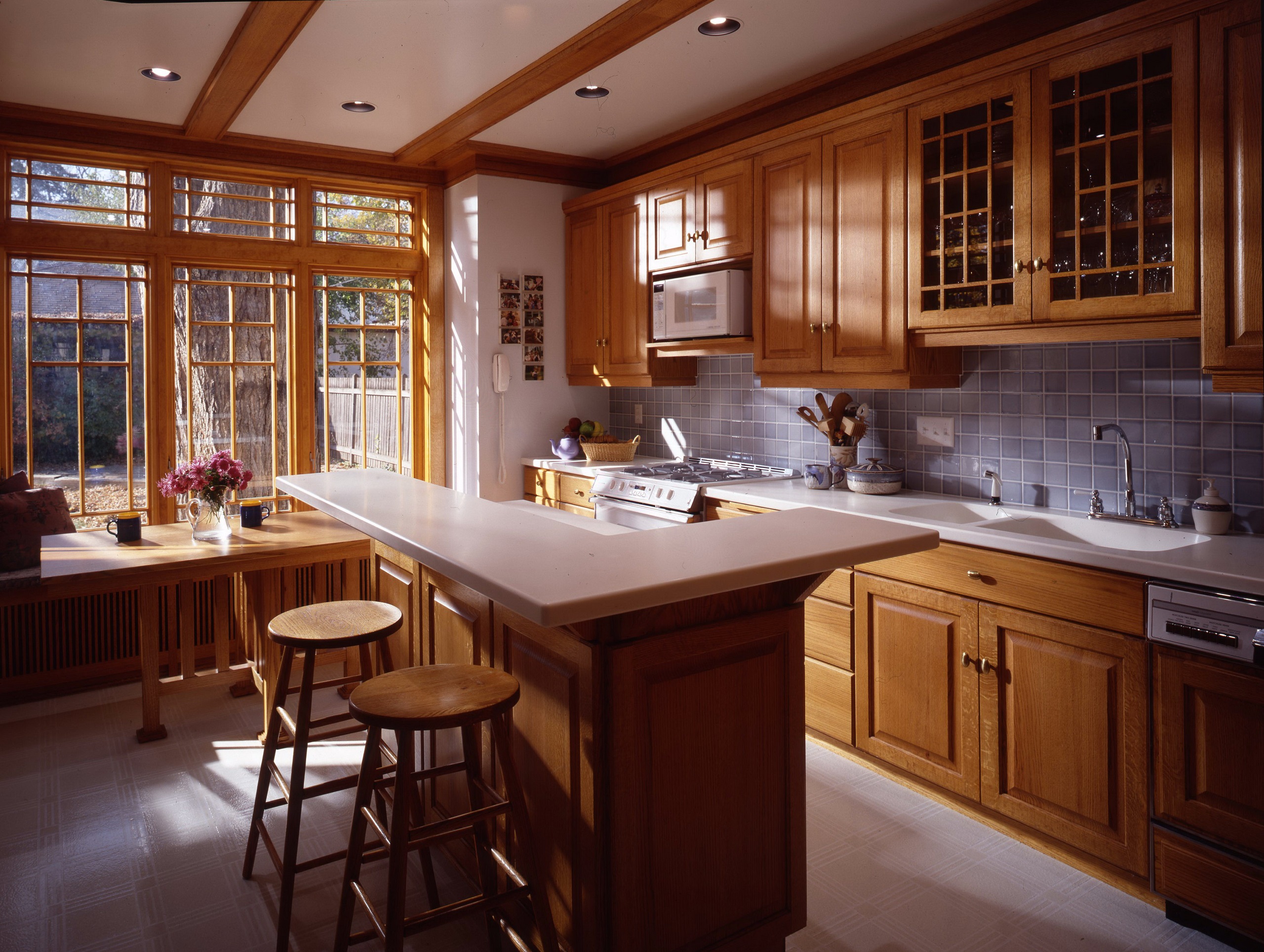 Large kitchen with white island, brown cabinets, big windows, and blue backsplash