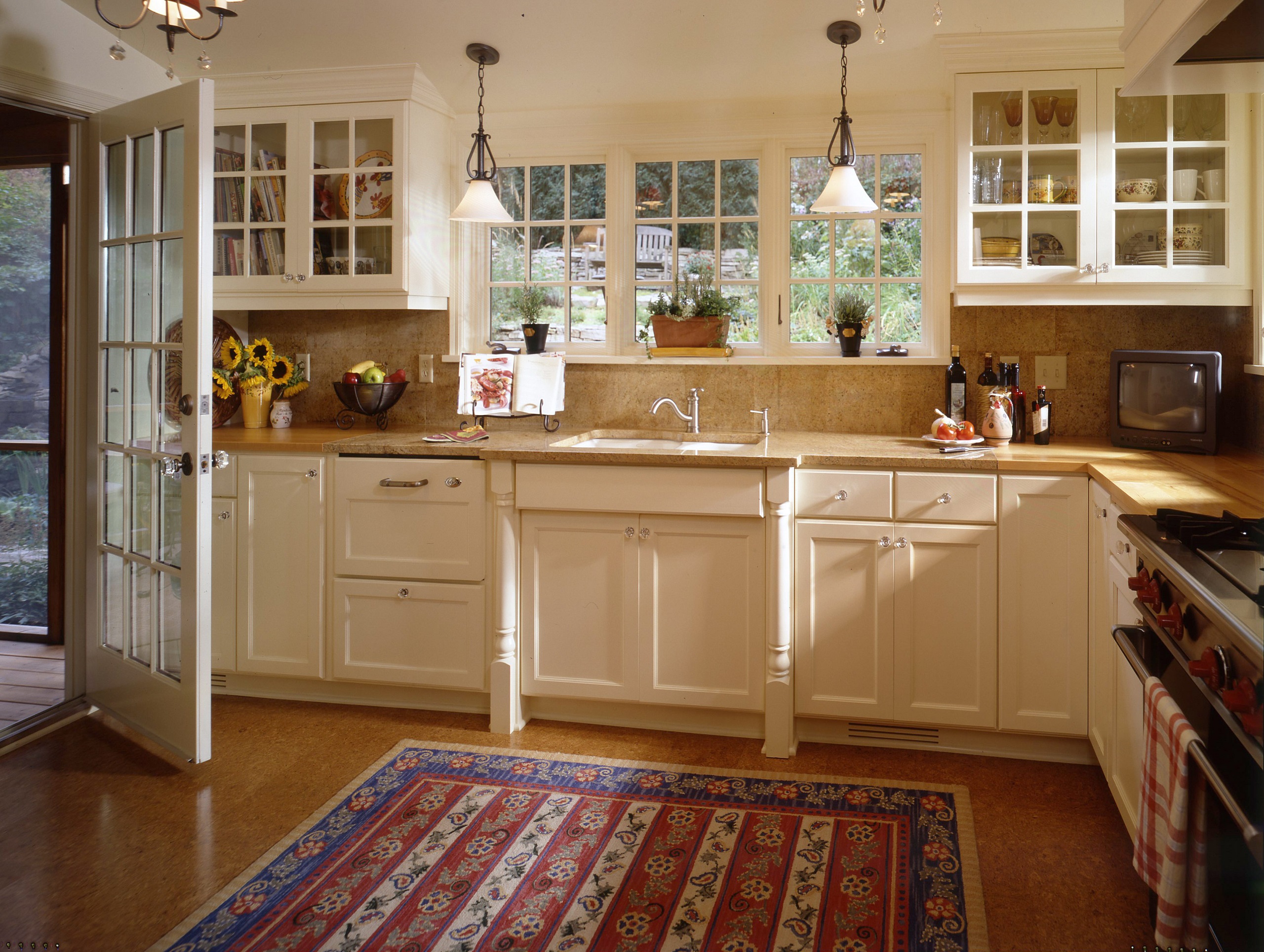 Remodeled kitchen with white cabinets, windows, lights, and a colored rug.